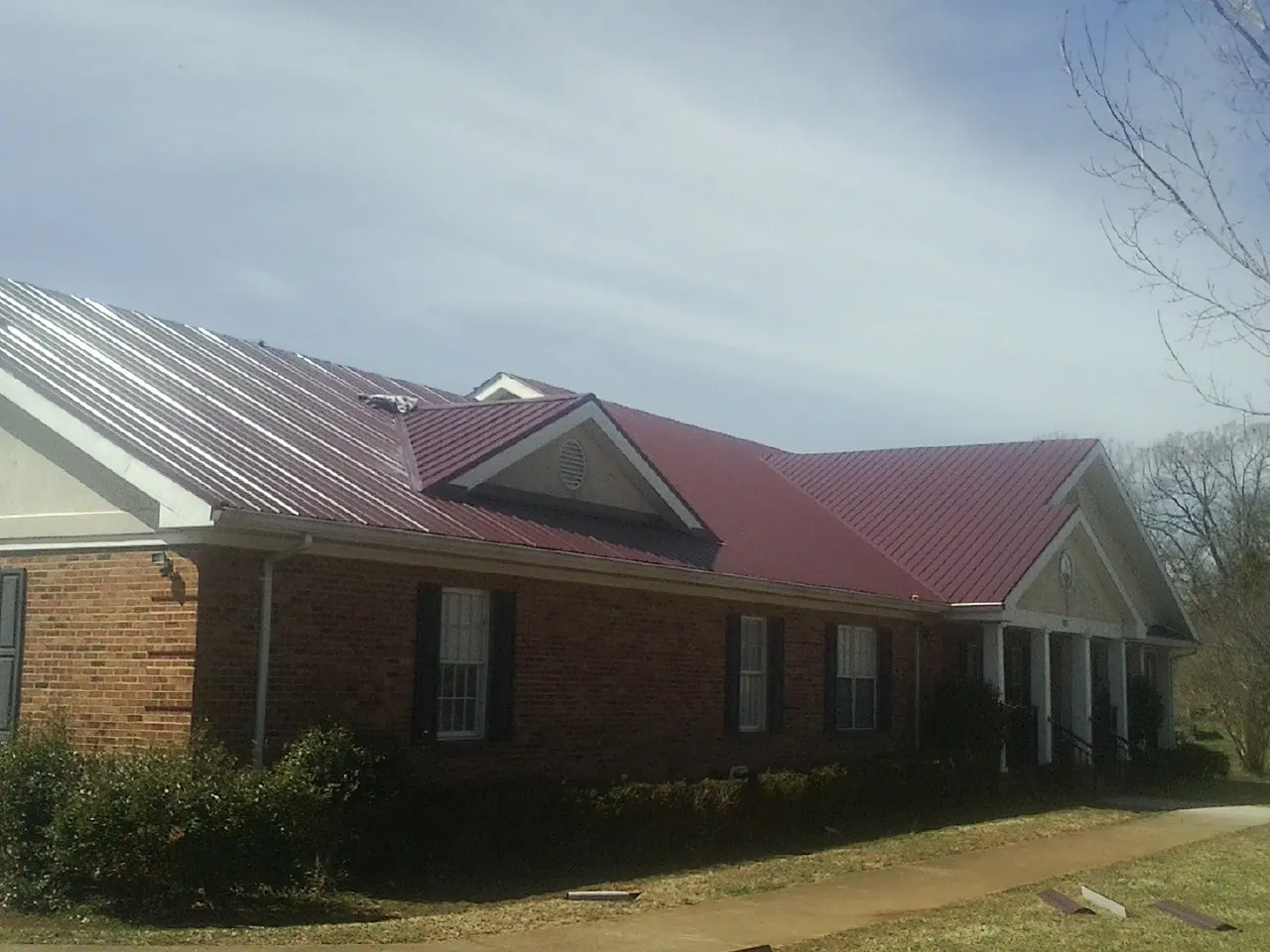 Red metal roof with gabled entries on a long brick building, from a Hail Damage Roof Repair job in Girdletree