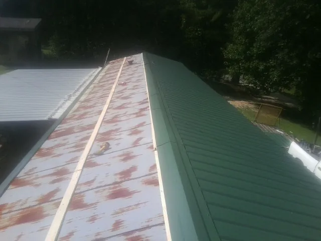 Old rusted panels beside newly installed green metal roofing — Wind Damage Roof Repair by Roofing Brothers in Girdletree