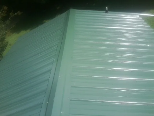 New green metal panels meeting at the ridge of a roof — Flat Roof Repair work by our crew in Girdletree