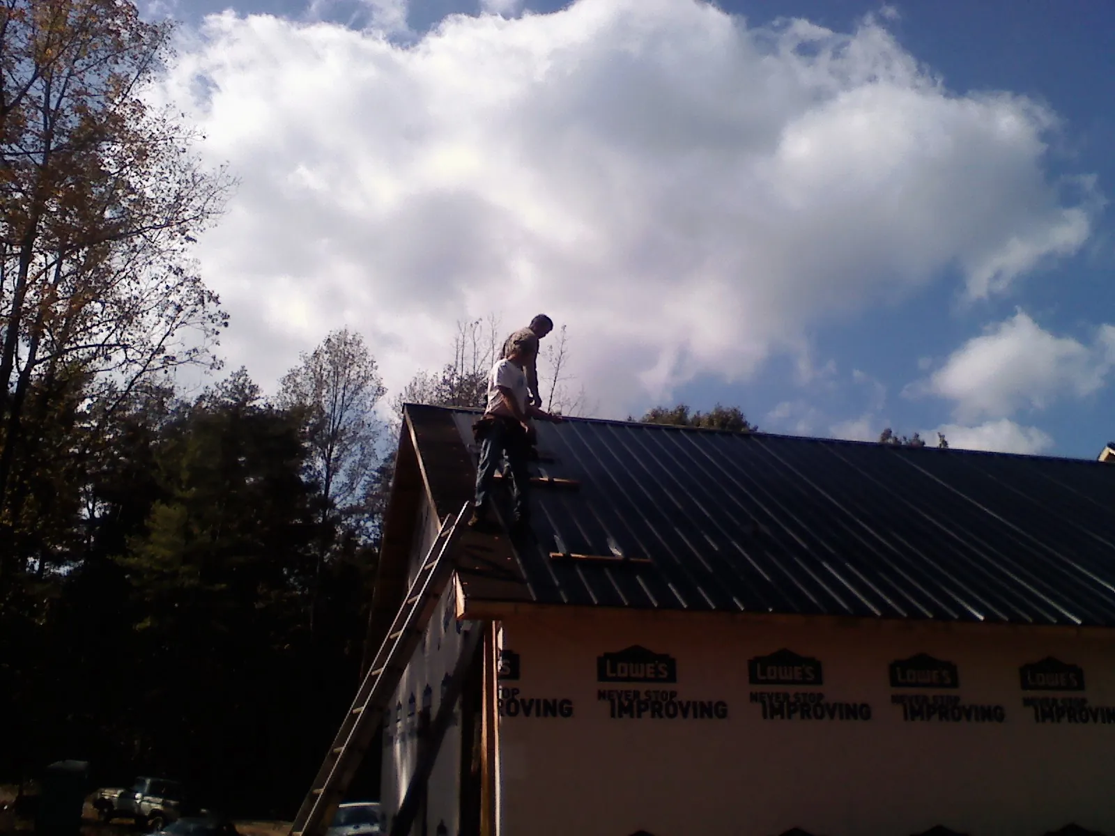 Roofer fastening dark metal panels high against a cloudy sky, from a Roof Inspection job in Girdletree