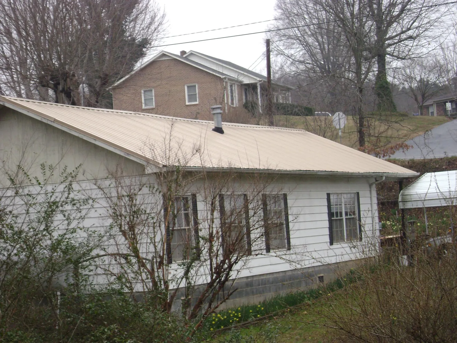 Tan metal roof on a white sided house set into a hillside — Commercial Roofing by Roofing Brothers in Girdletree